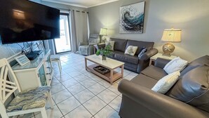 Una sala de estar con televisor de pantalla plana, sofá, mesa de centro y lámpara.