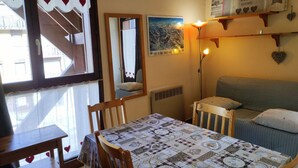 A cozy room with a dining table, chairs, a sofa, a mirror, and a wall with a poster and a shelf with decorative items. - Cozy Studio for 4 in Village Center, Near Slopes and Shops (Les Carroz d'Arâches)