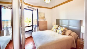 Een slaapkamer met een bed, een dressoir, een nachtkastje, een raam en een plafondventilator.