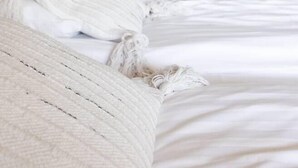 Un lit avec du linge de lit blanc, un oreiller blanc et une couverture blanche.