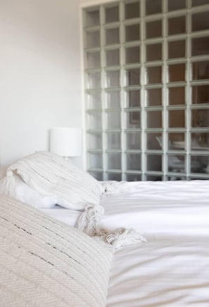 Un lit avec du linge de lit blanc, un oreiller blanc et une couverture blanche.