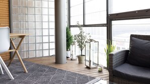 Un salon moderne avec une grande fenêtre, un canapé gris, une petite table et des plantes en pot.