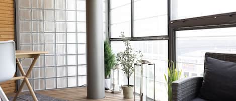 A modern living room with a large window, a grey sofa, a small table, and potted plants.