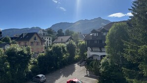 A parking lot with a red car, surrounded by trees and buildings with a mountain in the background. - Cozy Mezzanine Studio in Village Center with Balcony (Villard-de-Lans)