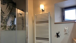 Ein Badezimmer mit Duschkabine aus Glas, einem weißen Handtuchhalter und einer wandmontierten Leuchte.