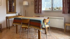 A dining area with a table covered by a striped tablecloth, surrounded by wooden chairs. - Cozy Apartment with Balcony, WiFi, and Free Parking near Ski Slopes (Villard-de-Lans)