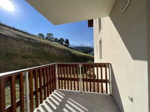 A balcony with a view of a grassy hill and mountains in the distance.