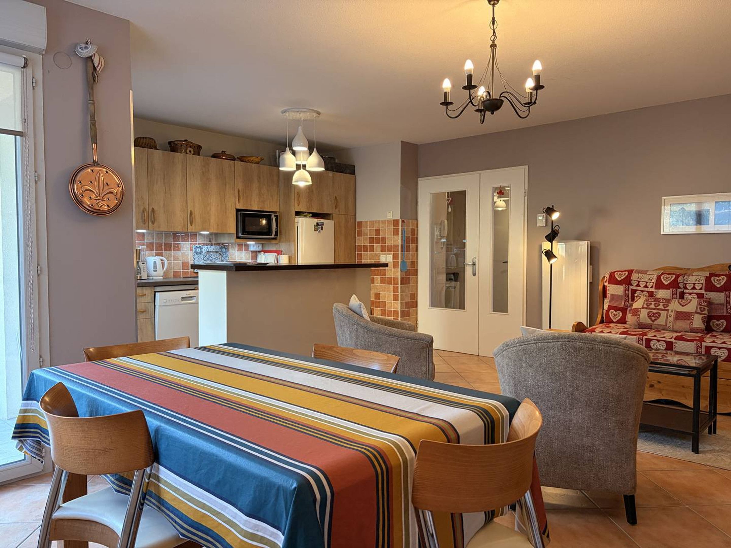 Une cuisine moderne avec des meubles en bois, un four à micro-ondes et un réfrigérateur. On y trouve également un coin repas avec une nappe à rayures et des chaises.