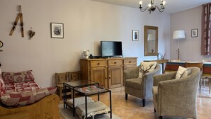 A cozy living room with a sofa, armchairs, a coffee table, and a TV on a wooden cabinet. - Cozy Apartment with Balcony, WiFi, and Free Parking near Ski Slopes (Villard-de-Lans)