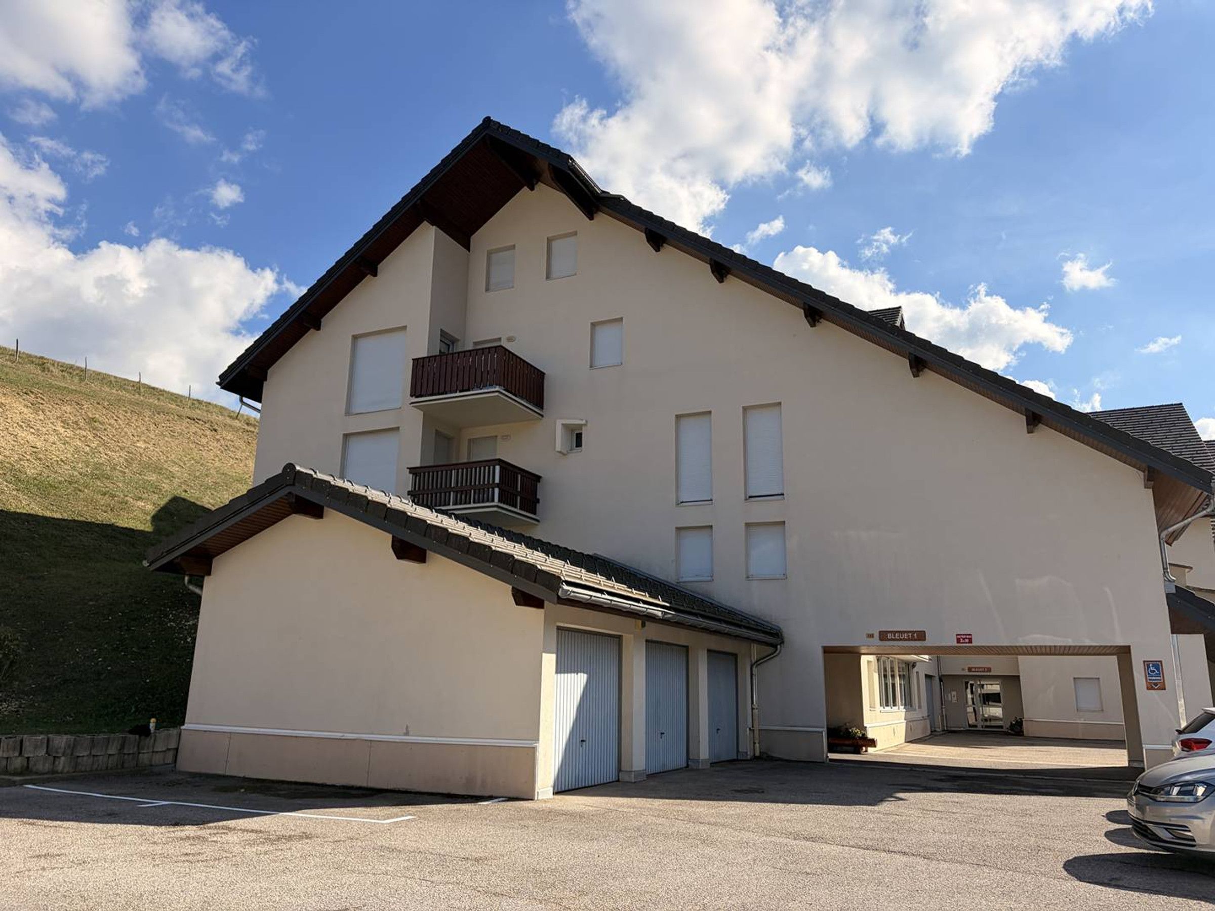 Ein mehrstöckiges Gebäude mit einem geneigten Dach, einem Balkon im zweiten Obergeschoss und einem Garageneingang.