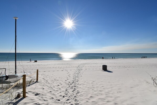 A beach with a clear sky, a bright sun, and footprints in the sand.