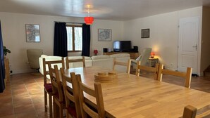 A dining area with a wooden table and chairs, a television in the background, and a window with curtains. - Spacious and functional house - 5 bedrooms, terrace, private parking (Villard-de-Lans)