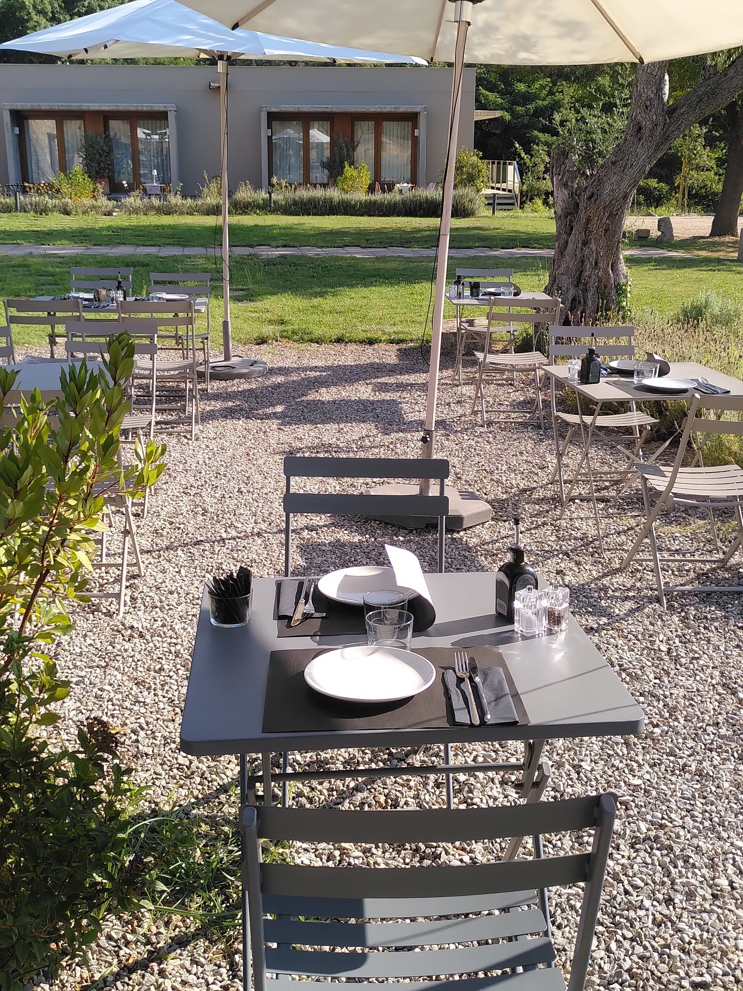 Un área de comedor al aire libre con mesas y sillas, un paraguas grande y un edificio al fondo.