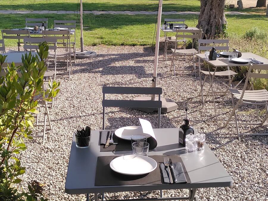 Un espace extérieur aménagé pour les repas, avec des tables et des chaises, un grand parasol, et un bâtiment en arrière-plan.
