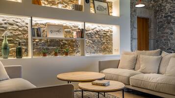 A cozy living room with a stone wall, a sofa, two round tables, and a bookshelf filled with books and framed pictures.