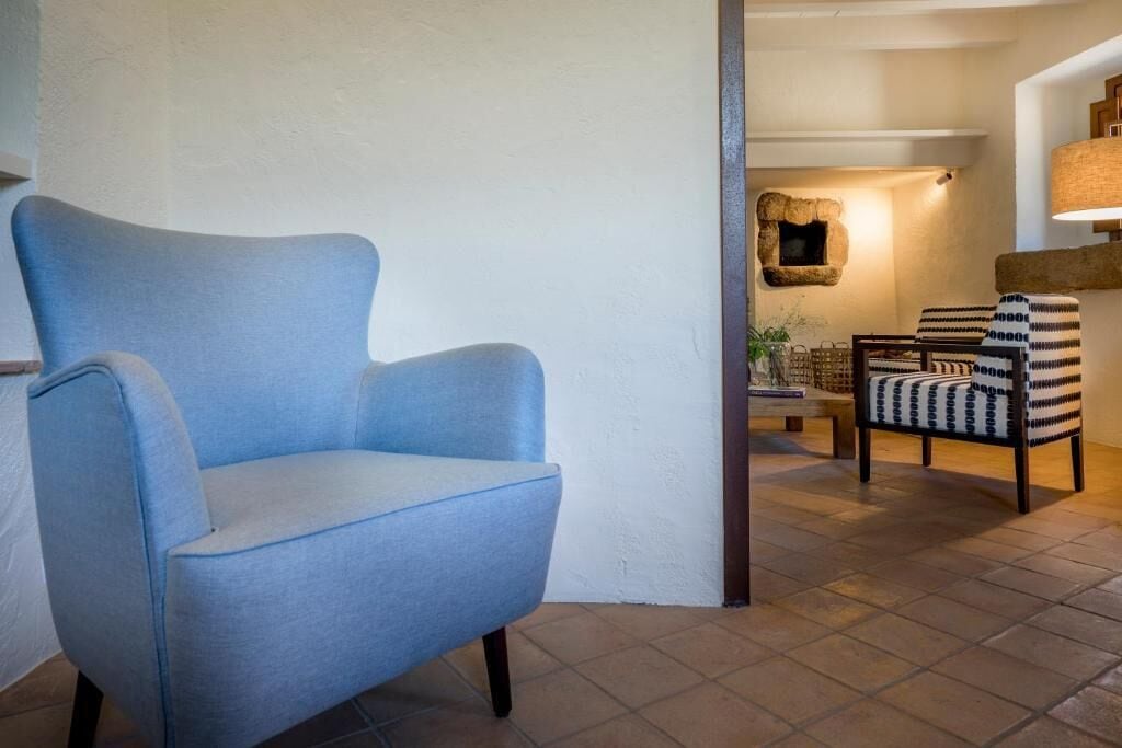 Een kamer met een blauwe fauteuil, een gestreept fauteuil en een kleine tafel met een lamp.