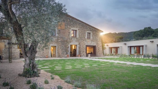 Un edificio de piedra con un patio, un árbol y vistas a una colina.