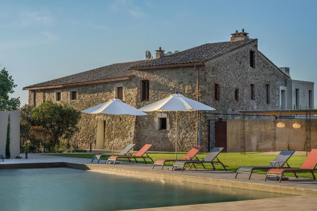 A stone building with a swimming pool, outdoor seating, and umbrellas.