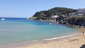 Una playa con aguas transparentes, un bote y edificios en una colina.