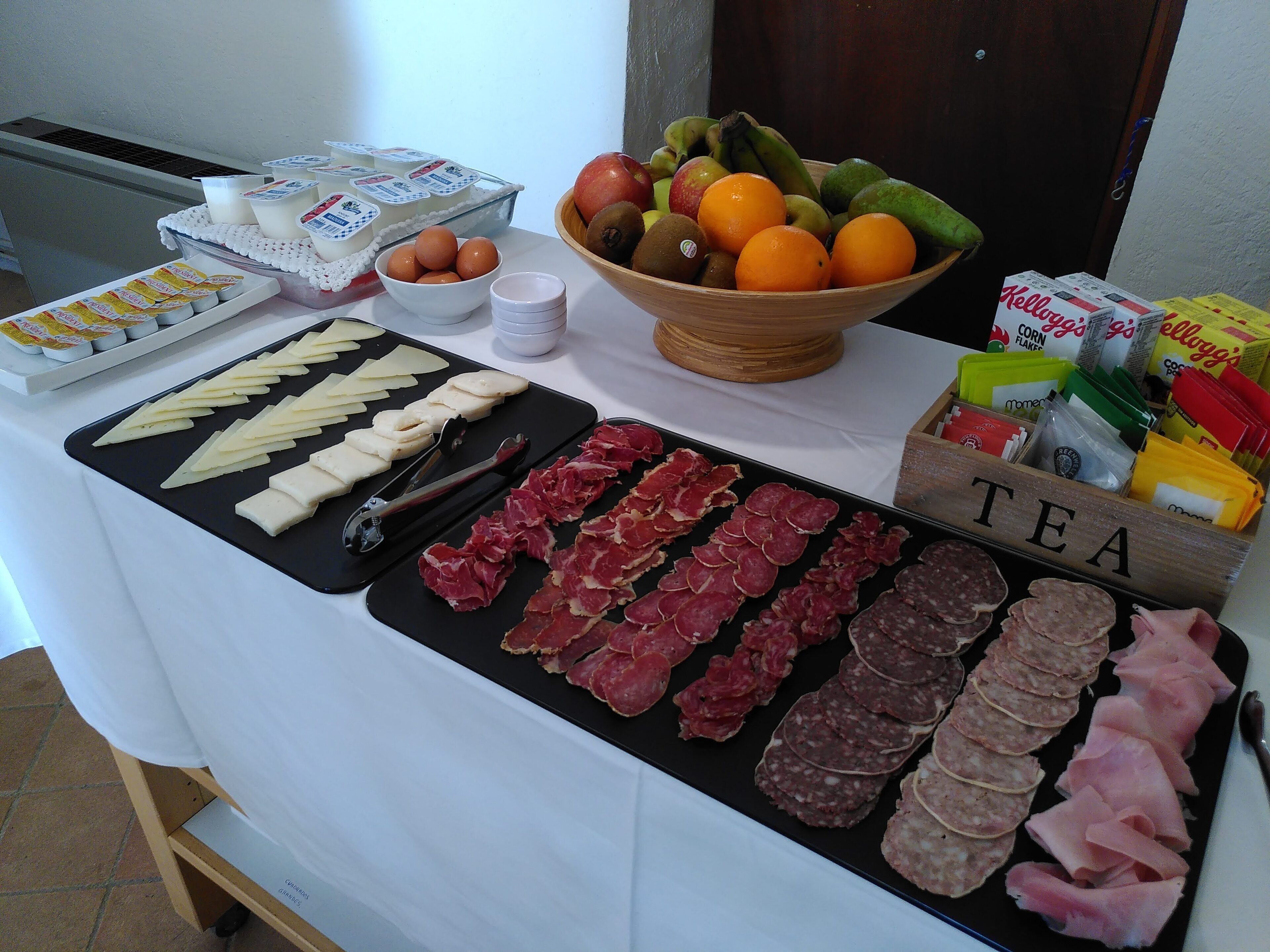 En buffet med forskellige retter, herunder kød, oste, frugt og drikkevarer.