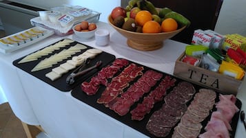 En buffet med forskellige retter, herunder kød, oste, frugt og drikkevarer.