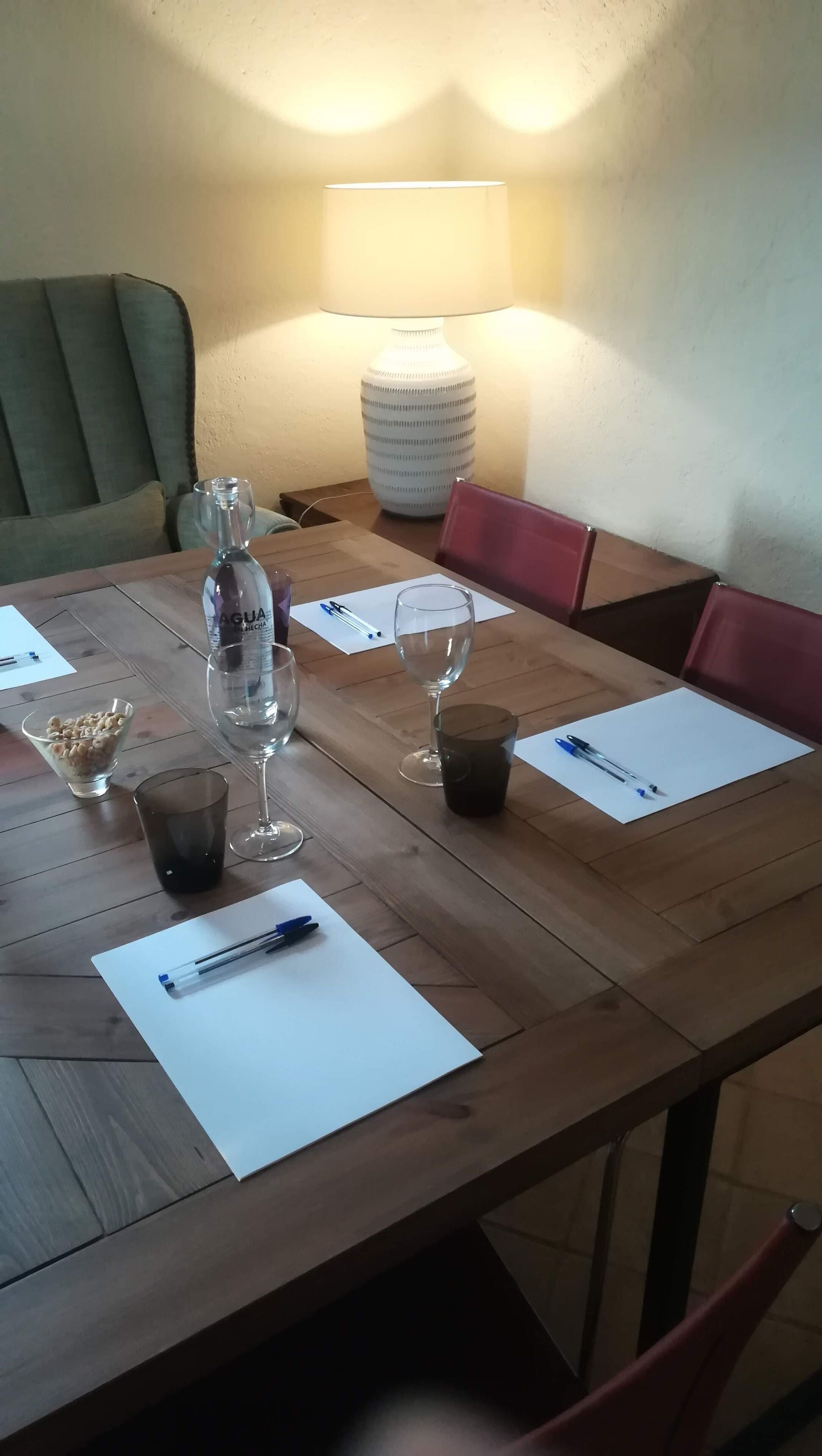 Una mesa de madera con una botella de agua, un vaso, un cuenco de cereal y un bolígrafo sobre un papel.