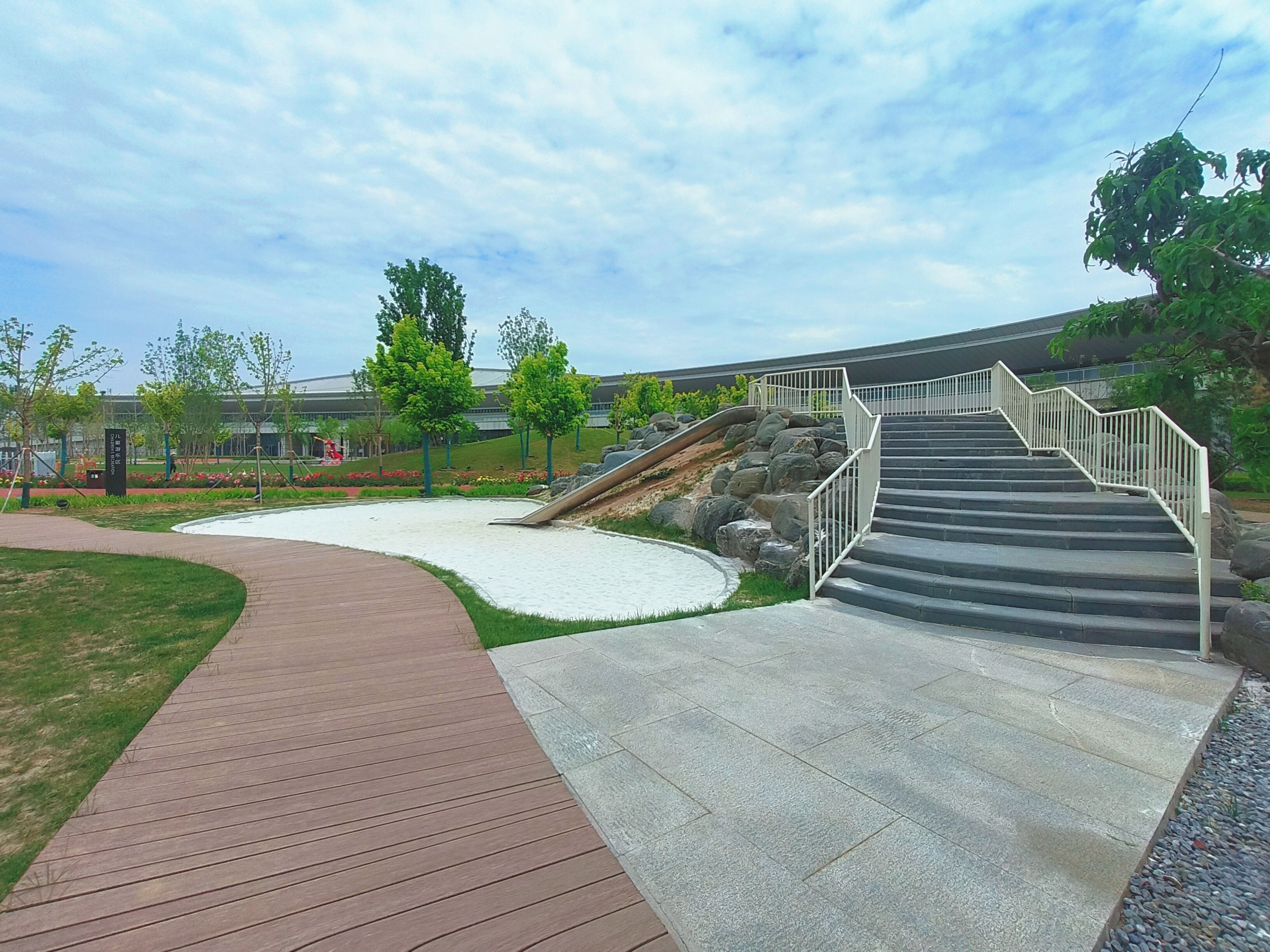 A modern outdoor area with a wooden pathway, stone steps, and a landscaped garden with trees and rocks.