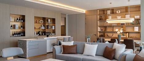 A modern living room with a grey sofa, a marble coffee table, and a kitchen area with wine bottles.