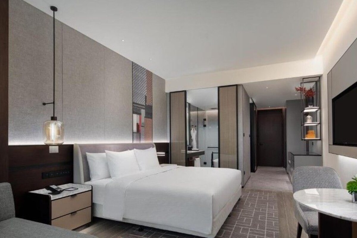 Una habitación de hotel moderna con una cama grande, mesitas de noche, un escritorio y un espejo.
