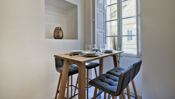 Een eetgedeelte met een houten tafel voor vier personen, twee stoelen en een vaas aan de muur.