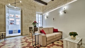 Een woonkamer met een beige bank, rode kussens, een salontafel en een potplant.