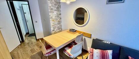 A compact living space with a dining area, a sofa, a mirror, and a view of the outside.