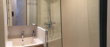 Un baño moderno con ducha envuelta en vidrio, un lavabo blanco y armarios de madera.