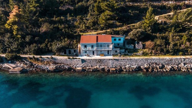 A coastal house with a red roof, situated next to a rocky shoreline. - Solar House Babina 1 (Korcula)