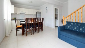 A modern kitchen with white cabinets, a dining table with chairs, and a blue sofa in a living area. - Solar House Babina 1 (Korcula)