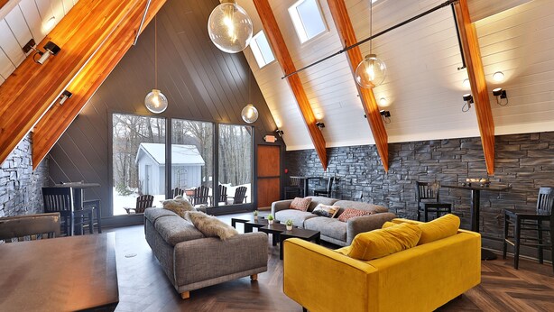 A spacious loft-style living area with high ceilings, exposed wooden beams, and large windows.