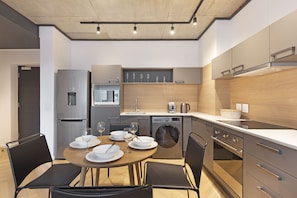 A modern kitchen with a dining area, stainless steel appliances, and a built-in oven. - Bridgewater View 415 by HostAgents  (Cape Town)