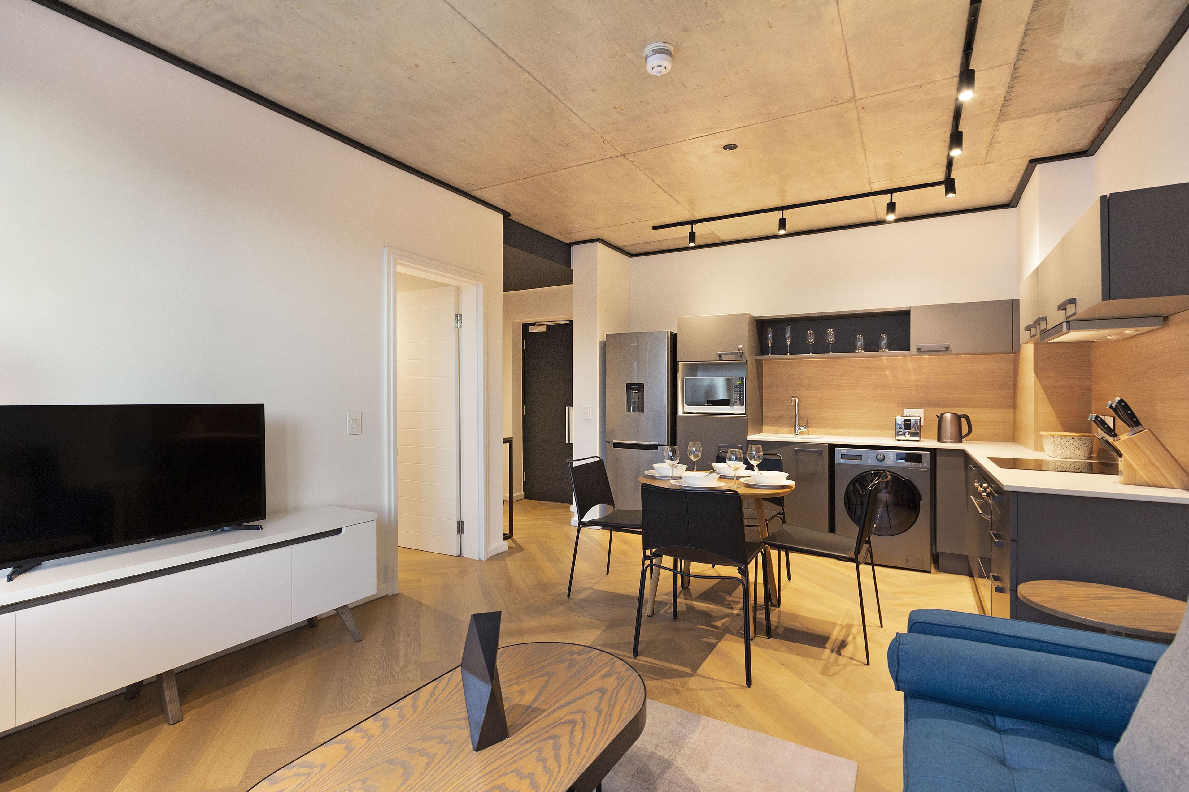 Una sala de estar moderna con un televisor de pantalla plana, una mesa de centro de madera y un sofá azul.