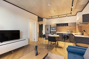 A modern living room with a flat-screen TV, a wooden coffee table, and a blue sofa. - Bridgewater View 415 by HostAgents  (Cape Town)