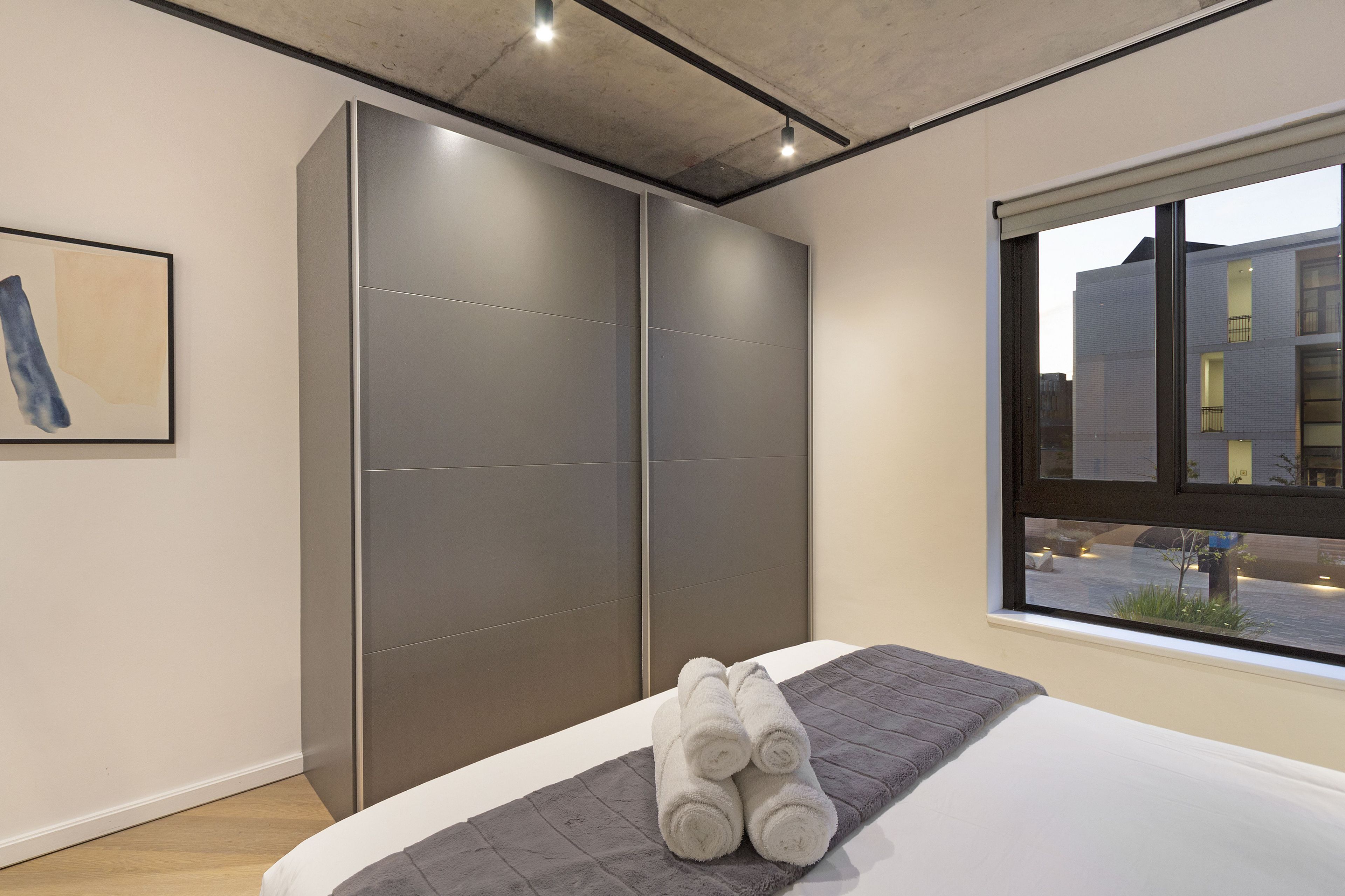 Un dormitorio moderno con una cama grande, cortinas grises y una ventana con vistas a la ciudad.