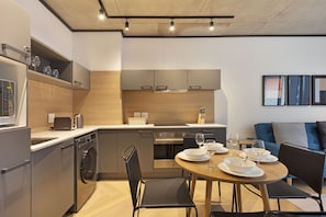 A modern kitchen with built-in appliances, a dining area with a round table, and a living space with a sofa.