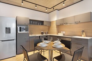 A modern kitchen with a built-in microwave, oven, and coffee maker. There is a dining table with chairs and a set of wine glasses.