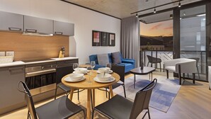 A modern kitchen with stainless steel appliances, a dining area with a round table and chairs, a blue sofa, and a balcony with a view of the sunset.