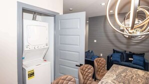 Un lavadero con lavadora, una puerta, una zona de estar con mesa y una lámpara colgante.
