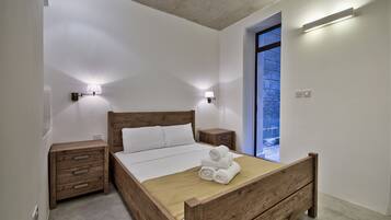 Ein Schlafzimmer mit einem hölzernen Bett, zwei Nachttischen, einem Beistelltisch und einem großen Fenster mit Blick auf einen blauen Himmel.