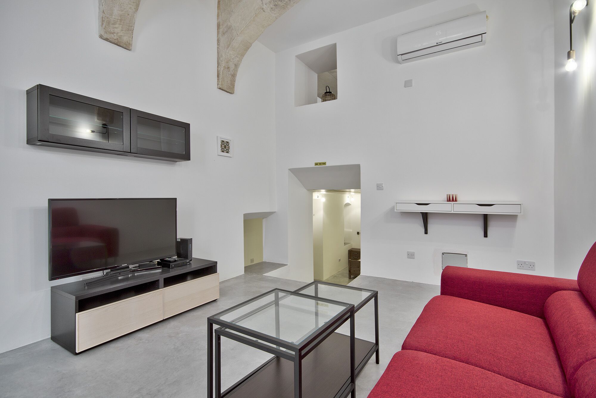 Una sala de estar moderna con un televisor de pantalla plana, una mesa de centro de vidrio y un sofá rojo.