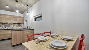 A modern kitchen with wooden cabinets, a tiled backsplash, and a dining area with a wooden table set for four. - Vallettastay - Casa Zoe  (Valletta)