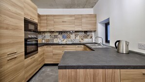 A modern kitchen with wooden cabinets, a black countertop, and a tiled backsplash. - Vallettastay - Casa Zoe  (Valletta)