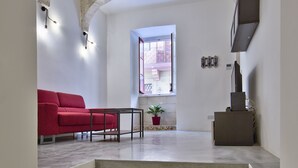 A modern interior with a red sofa, a small table, and a staircase leading to an upper level. - Vallettastay - Casa Zoe  (Valletta)