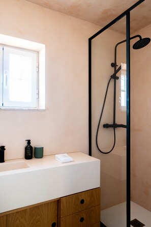 A modern bathroom with a glass-enclosed shower, a white vanity with a wooden cabinet, and a window above the sink. - SEA´YA Villa Areia with swimming pool and 5 minutes from the beach (Cascais)